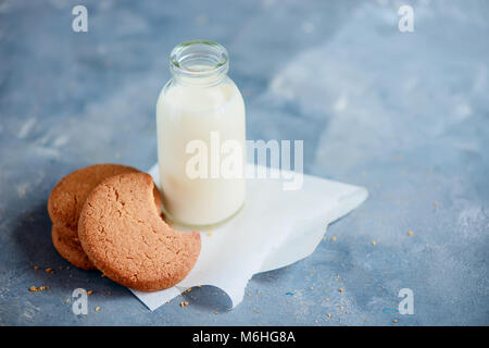 I cookie con segni di morsi e una bottiglia di latte su una luce blu tavolo da cucina con copia spazio. Sana colazione minimalista. Foto Stock