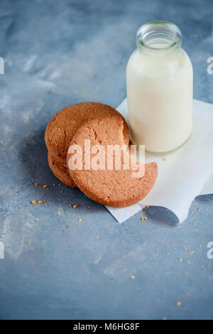 Sana colazione minimalista con farina di avena i biscotti con segni di morsi e una bottiglia di latte su una luce blu tavolo da cucina con copia spazio. Foto Stock