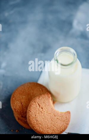 I cookie con segni di morsi e una bottiglia di latte su una luce blu tavolo da cucina con copia spazio. Sana colazione minimalista. Foto Stock