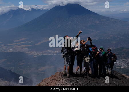 I turisti prendono selfies dopo aver raggiunto la cima del vulcano Pacaya con Fuego in background in Guatemala. Foto Stock