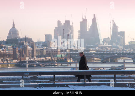 Un " commuter " passeggiate sulla neve coperto Waterloo Bridge con la City di Londra quartieri finanziari di grattacieli, la cattedrale di St Paul e edifici alti Foto Stock