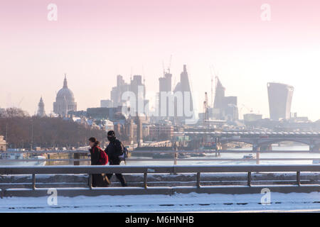 Un " commuter " passeggiate sulla neve coperto Waterloo Bridge con la City di Londra quartieri finanziari di grattacieli, la cattedrale di St Paul e edifici alti Foto Stock