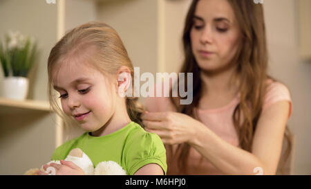 Madre premurosa trecciatura felice piccole figlie capelli, prendersi cura del suo bambino Foto Stock
