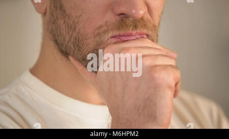 Close-up del giovane serio con la barba sfrega mento, avendo dubbi, pensando Foto Stock