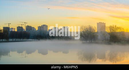 Pesante velatura su acqua in mattina. Skyline della città con edifici multipiano sulla banca del fiume Foto Stock
