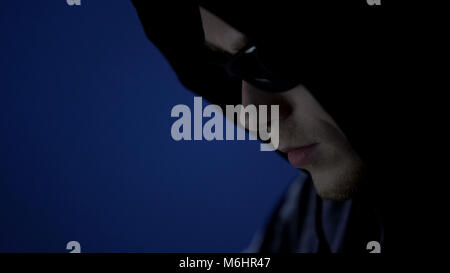 Ladro maschio in felpa con cappuccio e occhiali da sole, preparazione prima di reato, face close up Foto Stock