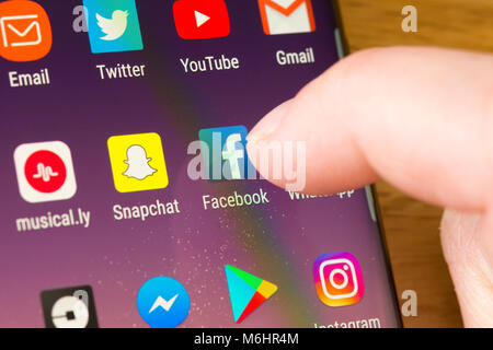 Primo piano dell'app Facebook su uno smartphone selezionato con il dito di una donna che punta verso l'app sul schermo del telefono cellulare Foto Stock