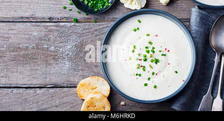 Il cavolfiore, crema di patate zuppa di cipolla verde in vaso nero su grigio Sfondo di legno. Copia dello spazio. Foto Stock