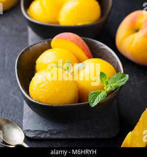 Mango, peach gelato e frutta tropicale sorbetti nella ciotola nero su sfondo di pietra. Foto Stock