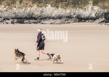 Un uomo e il suo cane che corre lungo una spiaggia. Foto Stock