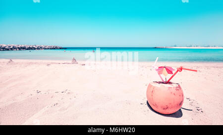 Retrò tonica ampio angolo di immagine di una noce di cocco con due cannucce e ombrello coloratissimo su una spiaggia, vacanze estate concetto, il fuoco selettivo. Foto Stock