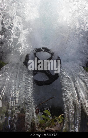 Potenza dell'acqua. L'acqua da una piccola cascata fluisce attraverso una grande ruota in ferro che è per la regolazione del flusso Foto Stock