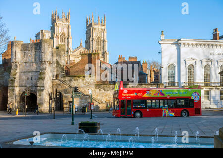 Un colore rosso brillante con sommità aperta double decker bus che porta i turisti in un tour intorno a York in Piazza dell'esposizione di fronte Bootham Bar e il Minster Foto Stock