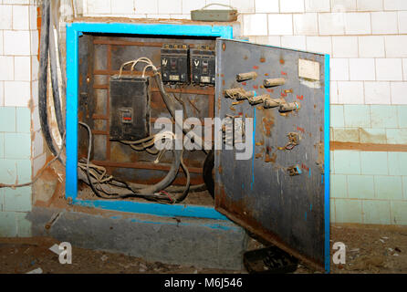 Smontaggio vecchie e arrugginite pannello elettrico complessivo su un abbandonato e distrutto la fabbrica contro uno sfondo di caos. Distruzione e atti di vandalismo. Ukrai Foto Stock