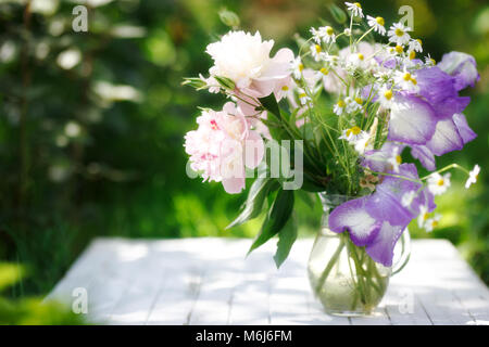 Bouquet di peonie bianco, chamomiles e iride fiori in vaso di vetro. Estate sfondo. Foto Stock