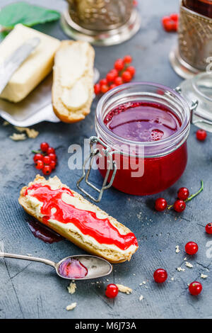 Un vasetto di ribes rosso marmellata di frutti di bosco e brioche Foto Stock