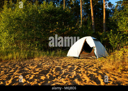 Tenda bianca in piedi presso una spiaggia camping posto al Lago Vänern in Svezia. Il sole splende e presto sarà il tramonto. Tenda è coperta da alberi e l'impianto. Foto Stock