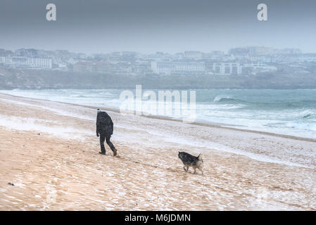 La caduta della neve come un uomo cammina con il suo cane attraverso Fistral Beach in Newquay Cornwall. Foto Stock