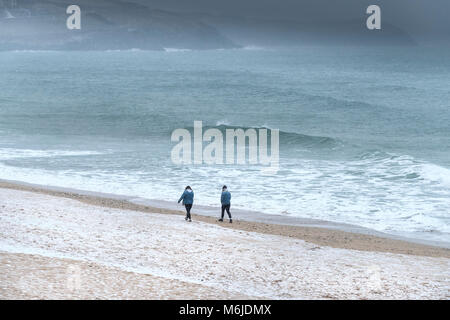 Due persone a piedi lungo Fistral Beach durante il congelamento invernale condizioni meteo in Newquay Cornwall. Foto Stock