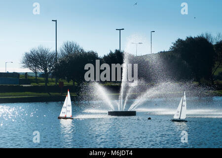 Modello di vela Barche a vela passato una fontana ornamentale Trenance sul lago in barca in Newquay Cornwall. Foto Stock