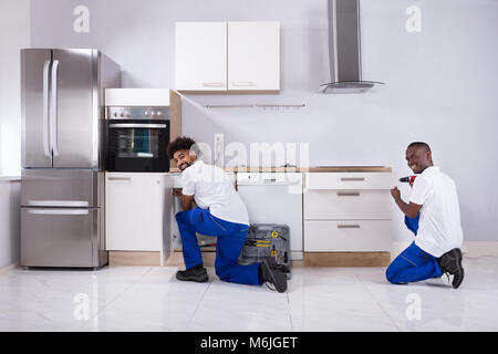 Vista posteriore di due giovani Handymen in uniforme che fissa i cabinet in legno in cucina Foto Stock