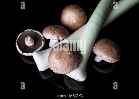 Porri e grandi funghi marrone su sfondo nero da sopra Foto Stock