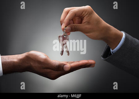 Close-up di mani che dà le chiavi di un appartamento contro uno sfondo grigio Foto Stock