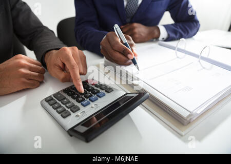 Close-up di due ragionieri calcolo fattura fiscale utilizzando la Calcolatrice sulla scrivania in ufficio Foto Stock