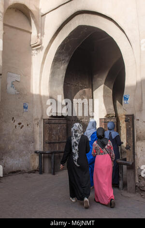 Quattro donne marocchine in abito tradizionale con testa sciarpe a piedi attraverso un arco nella medina di Marrakech, Marocco. Foto Stock