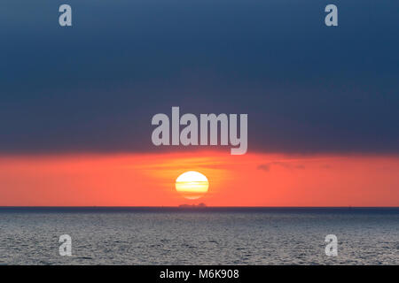 Inghilterra, Ramsgate. Alba sul Canale Inglese. Sun appena sopra l'orizzonte con molto nuvole scure sopra di esso. Silhouette di una grande nave da carico che passa direttamente al di sotto. Foto Stock