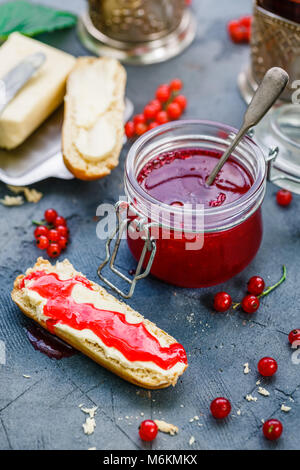 Un vasetto di ribes rosso marmellata di frutti di bosco e brioche Foto Stock