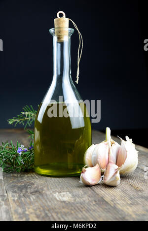 La bottiglia sul tavolo di legno contiene olio extra vergine di oliva prodotto in Italia. Aglio e rosmarino sono le erbe aromatiche Foto Stock