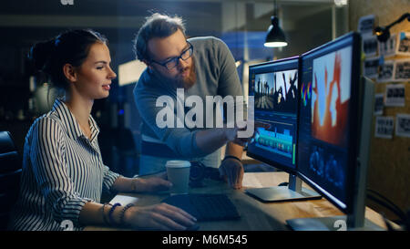 Video di sesso femminile e Sound Editor funziona con il suo collega di sesso maschile sul progetto sul suo personal computer con due schermi. Essi lavorano in Creative Ufficio Loft Foto Stock