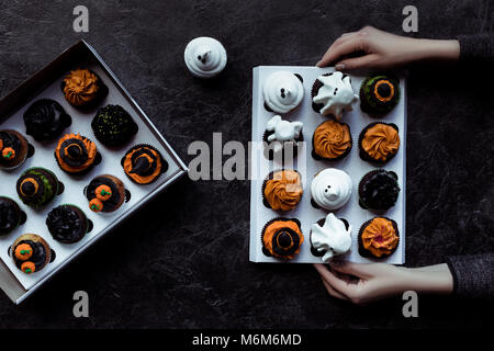 Vista dall'alto di mani umane della scatola di contenimento con una decorazione halloween tortine su nero Foto Stock