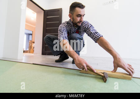 Uomo bello misurando il pavimento in legno con martello installare laminato Foto Stock