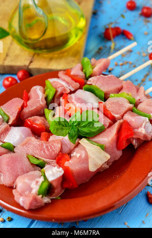 Primo piano di alcune materie di carne di tacchino Spiedini misti con verdure in un marrone piastra di terracotta, posto su un blu tavola in legno rustico con un ampolla con oli Foto Stock