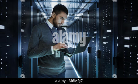 Tecnico che lavora su un computer portatile in grandi data center pieno di server Rack. Egli esegue il programma di diagnostica e manutenzione, Imposta sistema. Foto Stock