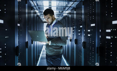 Tecnico che lavora su un computer portatile in grandi data center pieno di server Rack. Egli esegue il programma di diagnostica e manutenzione, Imposta sistema. Foto Stock