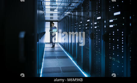 Tecnico IT funziona su computer portatile in grandi data center pieno di server Rack. Egli esegue il programma di diagnostica e manutenzione, Sistema di set up. Foto Stock