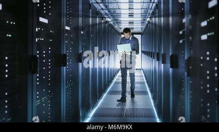 Tecnico IT funziona su computer portatile in grandi data center pieno di server Rack. Egli esegue il programma di diagnostica e manutenzione, Sistema di set up. Foto Stock