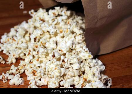 Burro fresco di popcorn si riversa fuori di un sacchetto di carta e su un tavolo di legno - Un film classico snack. Foto Stock