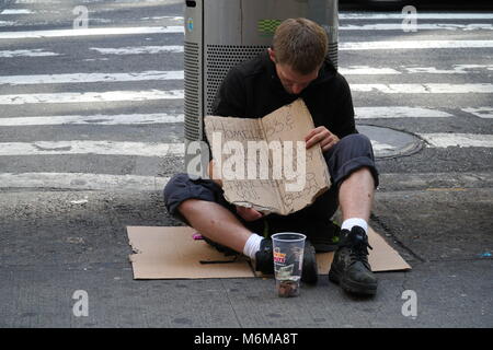 New York City - Settembre 2016: uomo senza tetto tenendo un cartello di cartone si siede accanto a un gargabe può in Manhattan con una tazza di denaro per chiedere aiuto da Foto Stock