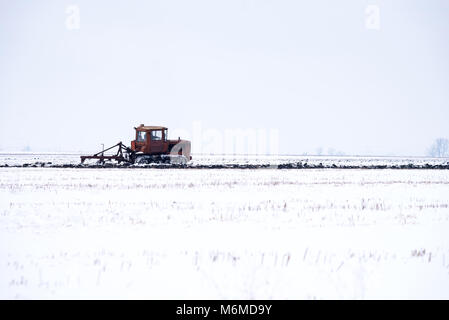 Trattore cingolato campo di aratura in inverno. Foto Stock