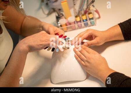 Close-up di una estetista e clienti di sesso femminile mani tenendo i campioni e la scelta di colori le unghie al salone di bellezza. Foto Stock