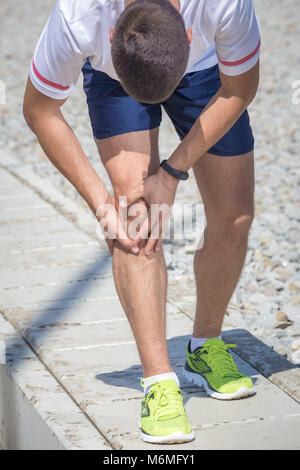 Esecuzione di atleta sentire dolore dopo avente il suo ginocchio infortunato. Incidente sulla via di corsa durante l'esercizio mattutino. Sport i concetti di incidente Foto Stock