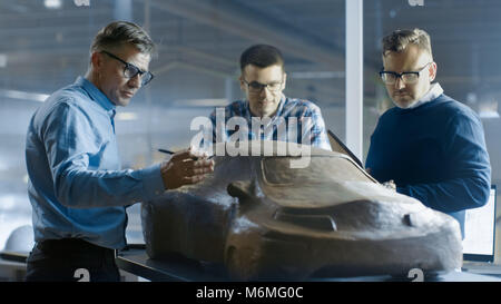 Il team di design automobilistico ingegneri discute un nuovo prototipo di modello fatto di plastilina Clay. Essi lavorano in una grande fabbrica di automobili. Foto Stock