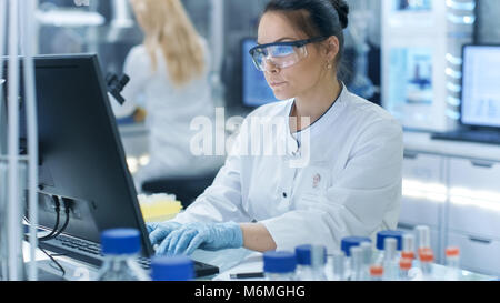 Medical Research Scientist digitando le informazioni ottenute dal nuovo farmaco sperimentale di prova. Lavora in un ambiente luminoso e moderno laboratorio. Foto Stock