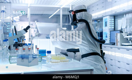 Virologia medica Research Scientist funziona in un Hazmat tuta con maschera, lei prende le provette dal frigo box. Lavora in un laboratorio sterile Foto Stock