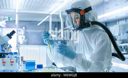 Virologia medica Research Scientist funziona in un Hazmat Suit con maschera, lei utilizza micropipetta. Lei lavora in una sterile High Tech Laboratory Foto Stock