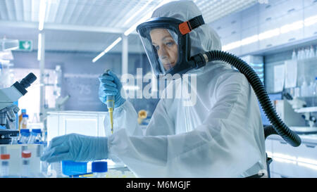 Virologia medica Research Scientist funziona in un Hazmat tuta con maschera, lei prende le provette dal frigo box. Lavora in un laboratorio sterile Foto Stock